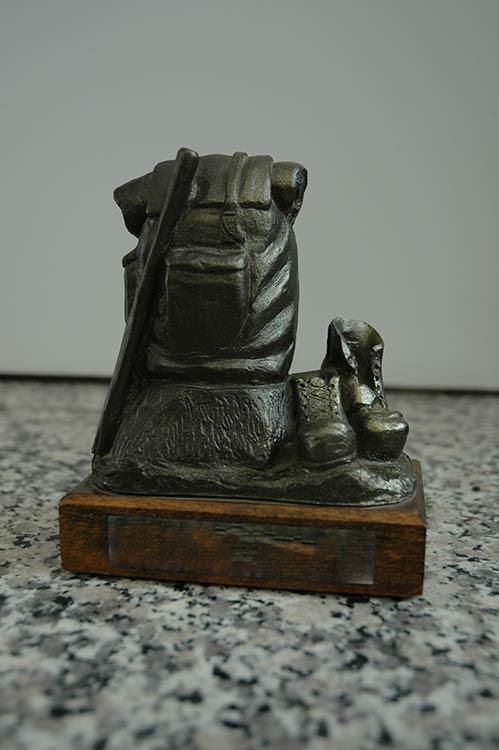 Eine kleine Statue einer Person mit Rucksack und Stiefeln auf einem Holzsockel.