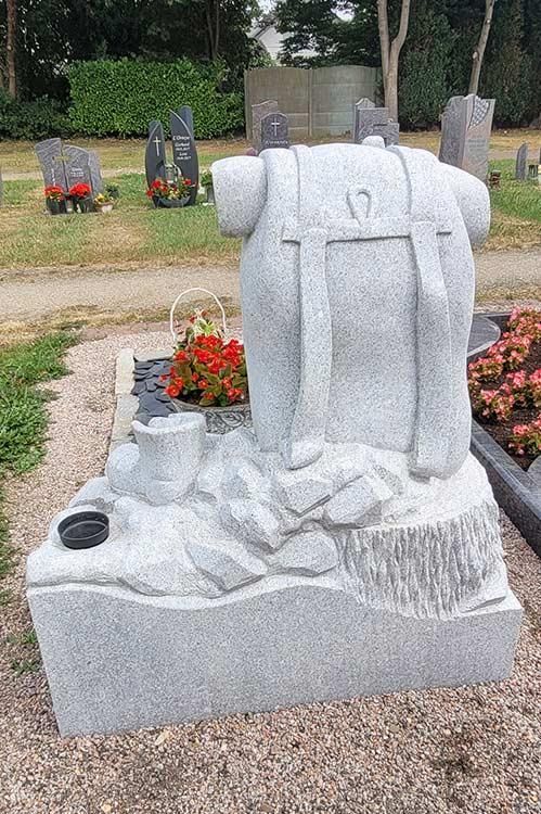 Ein Grabstein auf einem Friedhof mit einem Rucksack darauf.