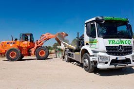 Un camión remolca una excavadora por un camino de tierra.