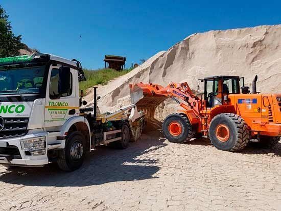 Un camión y una excavadora están estacionados frente a un montón de arena.