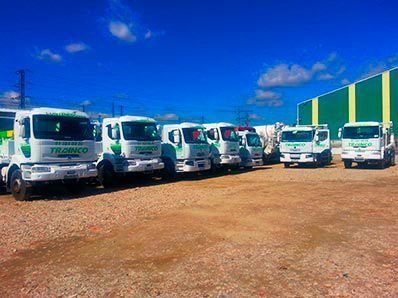 Una fila de camiones blancos están estacionados en un lote de tierra frente a un edificio verde.