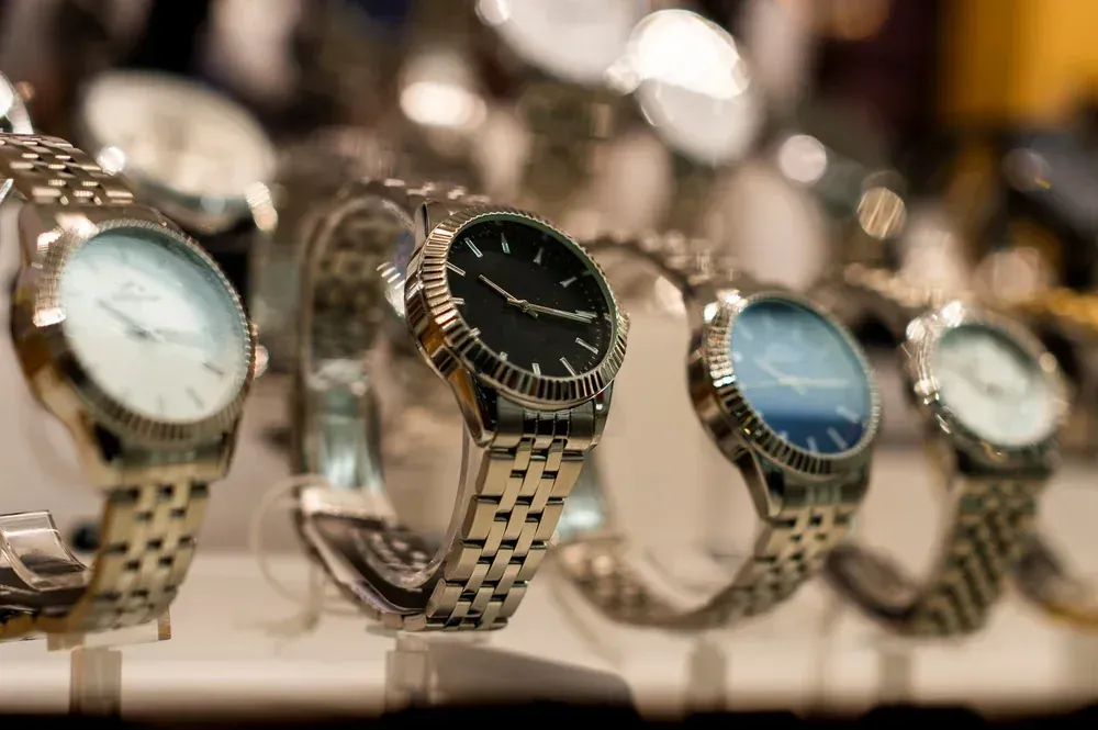 Relojes de pulsera expuestos en un estante, de diversos estilos con correas plateadas y esferas de diferentes colores.