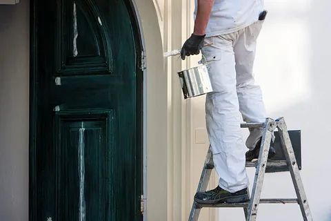 Un hombre está de pie en una escalera pintando una puerta.