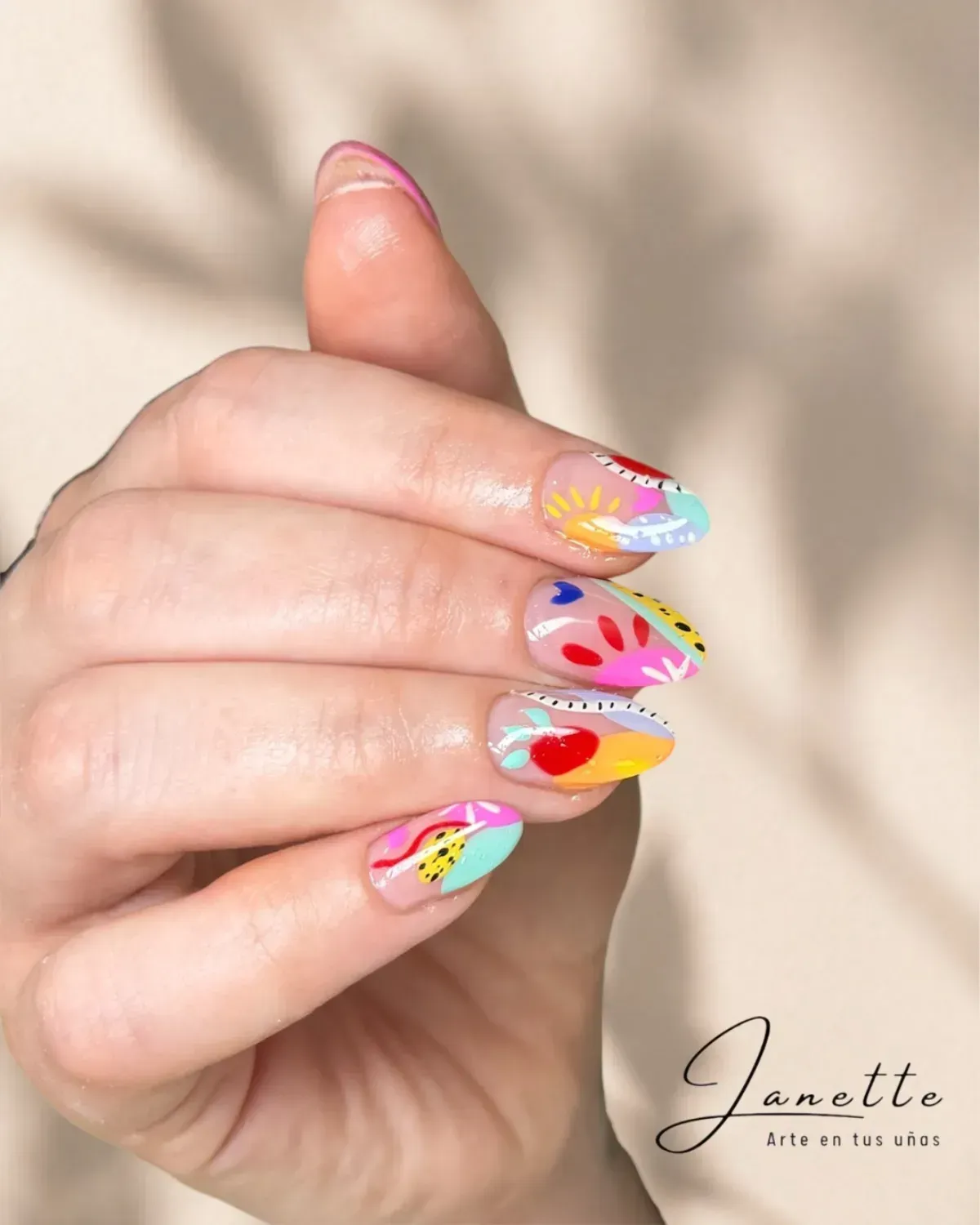 Mano con uñas largas decoradas con diseños de arcoíris en tonos pastel y coloridos diseños abstractos 