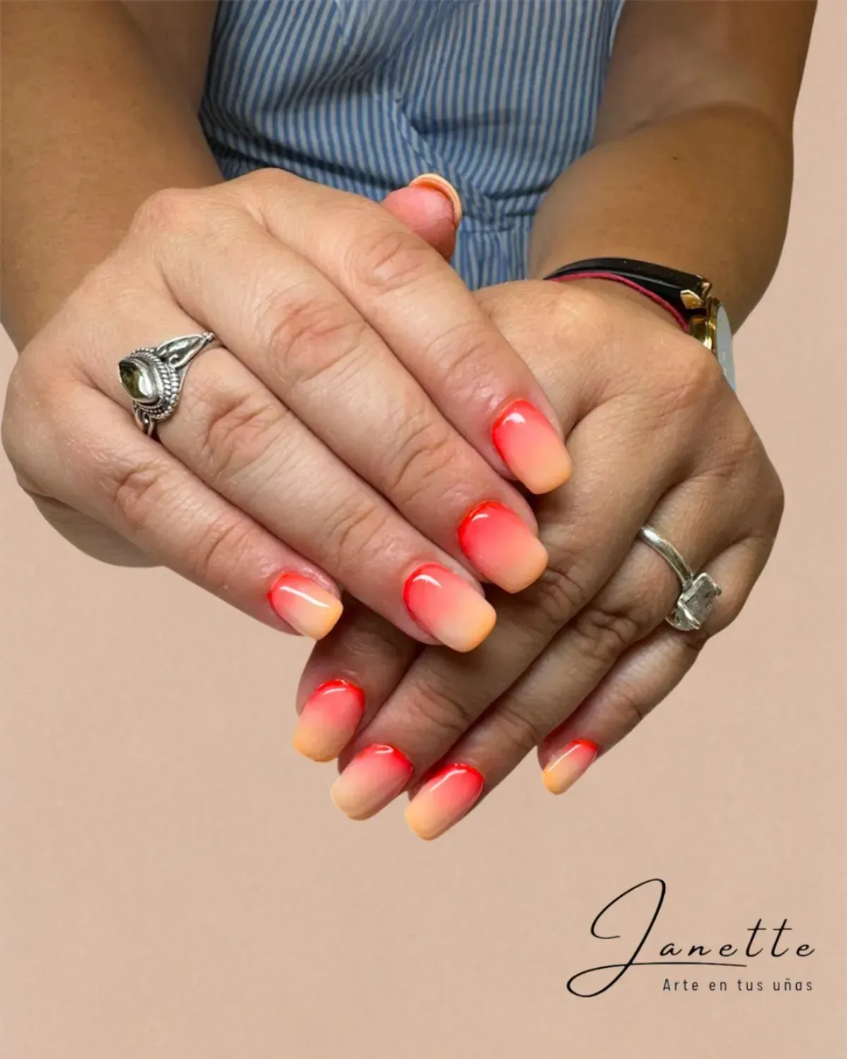 Manos con uñas y anillos en degradado rosa coral, descansando juntas sobre un fondo claro.