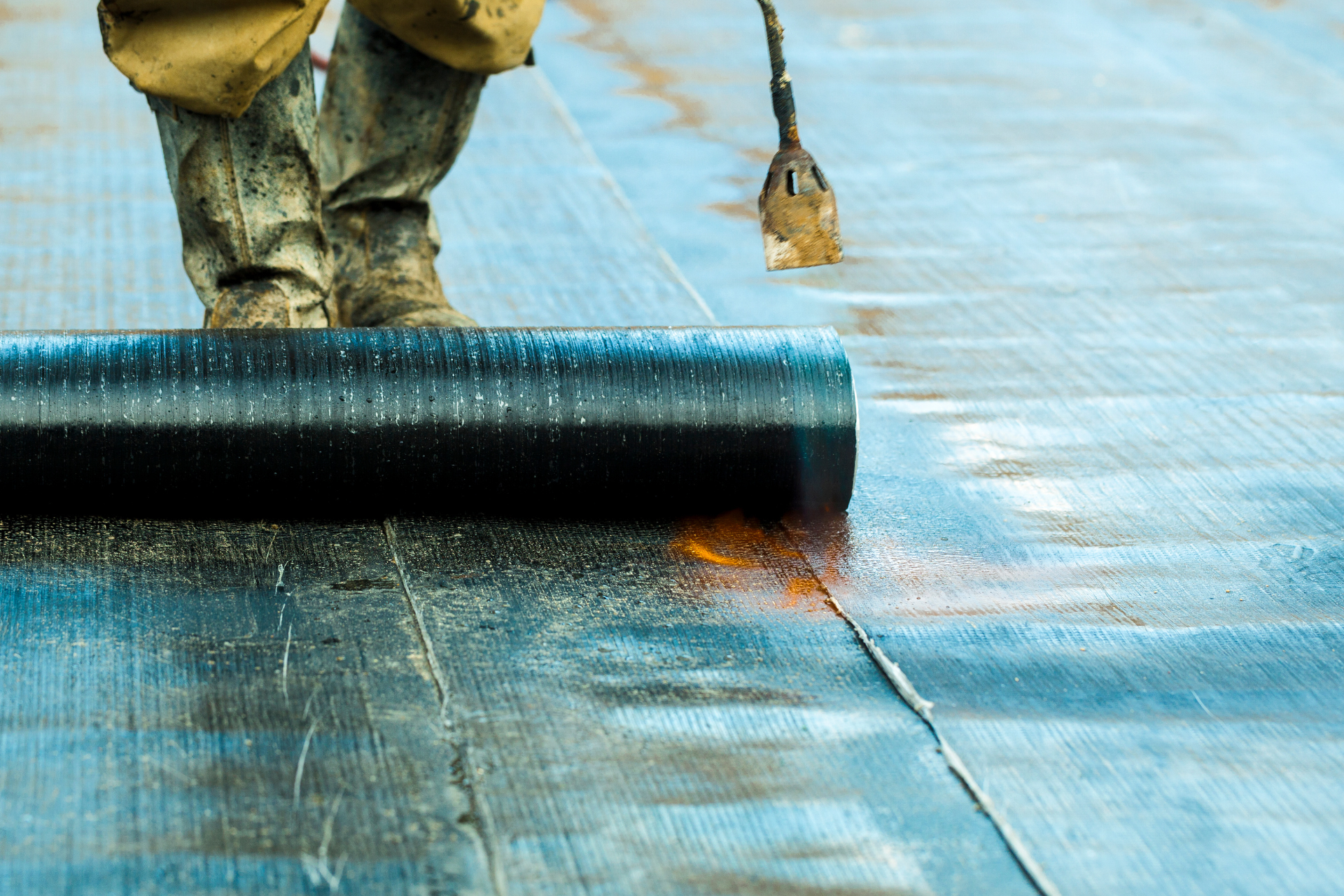Un techador utiliza un soplete para instalar un rollo de material para techos de color negro.