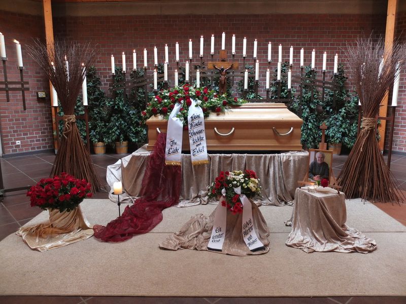 Ein Sarg steht mit Blumen und Kerzen auf einem Tisch in einer Kirche