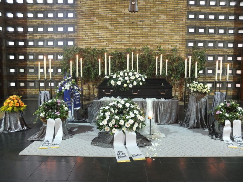 Eine Ausstellung von Blumen und Kerzen mit einem Sarg im Hintergrund