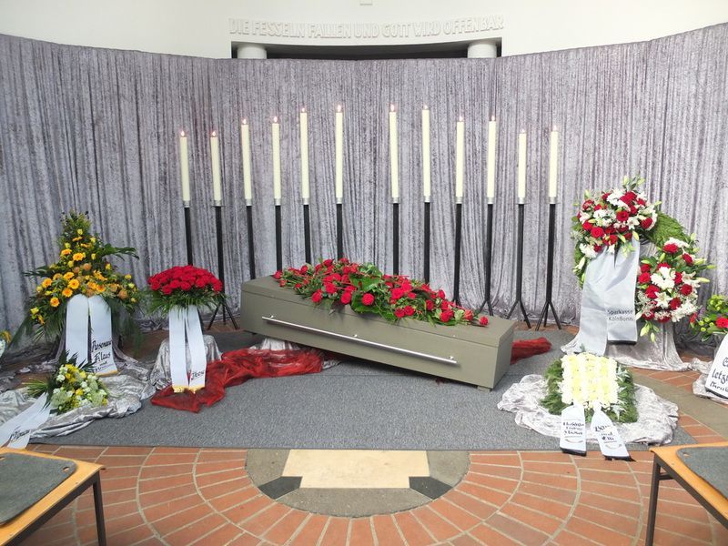 Ein Sarg mit Blumen und Kerzen vor einer Wand