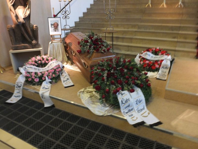 Ein Sarg ist von Blumen und einem Band mit der Nummer 12 umgeben