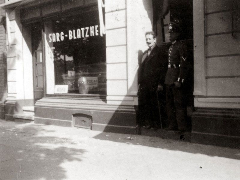 Ein Schwarzweißfoto von zwei Männern vor einem Laden namens Sarg-Blatzke