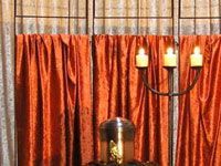 Ein Kerzenleuchter steht vor einem Fenster mit orangefarbenen Vorhängen.