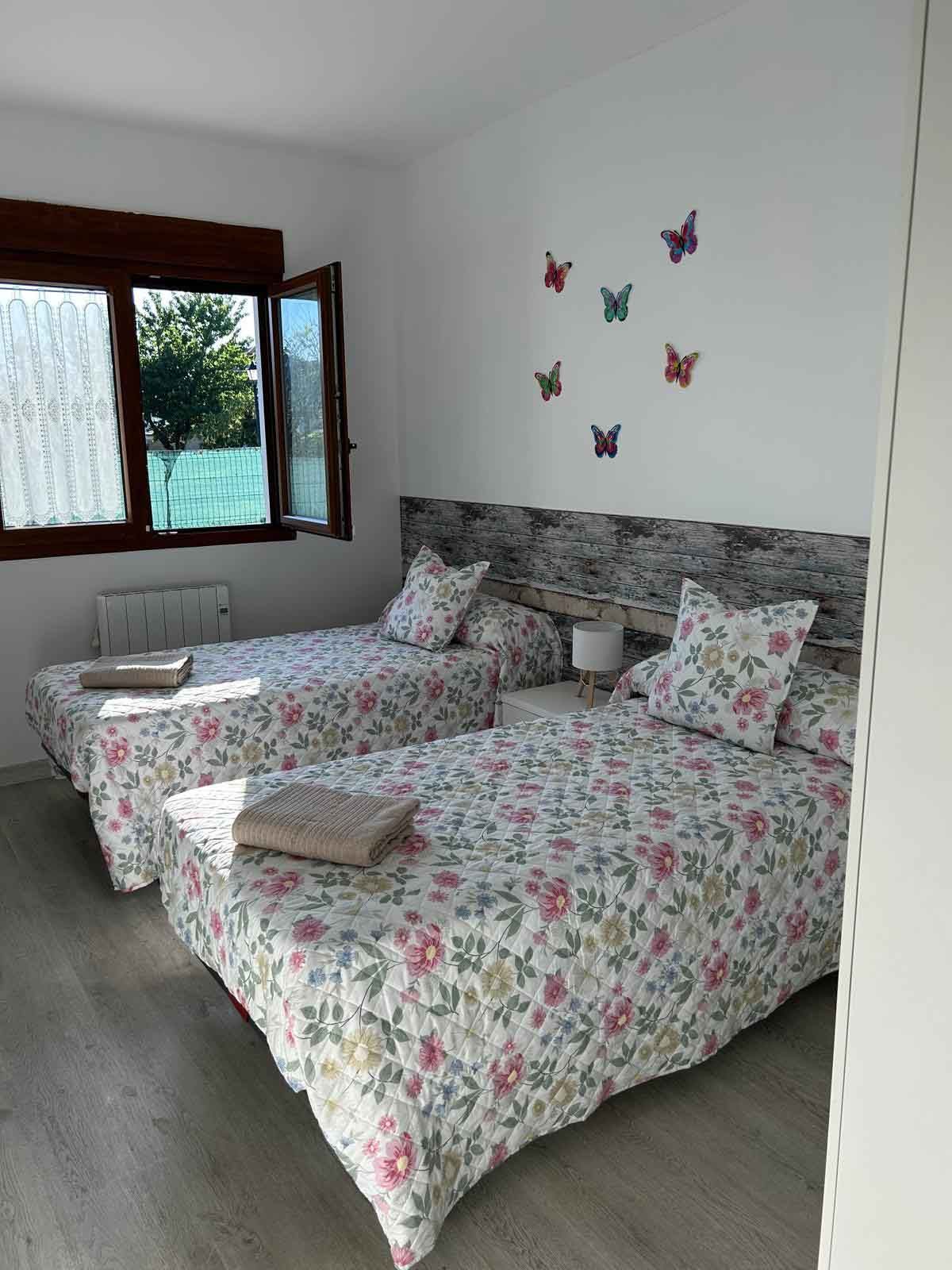 Un dormitorio con dos camas y una ventana con mariposas en la pared.