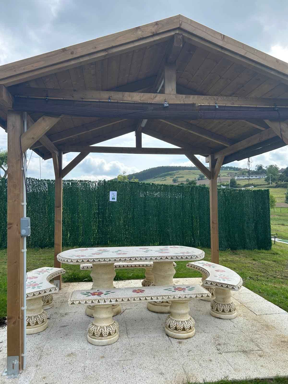 Un cenador de madera con una mesa y bancos debajo.