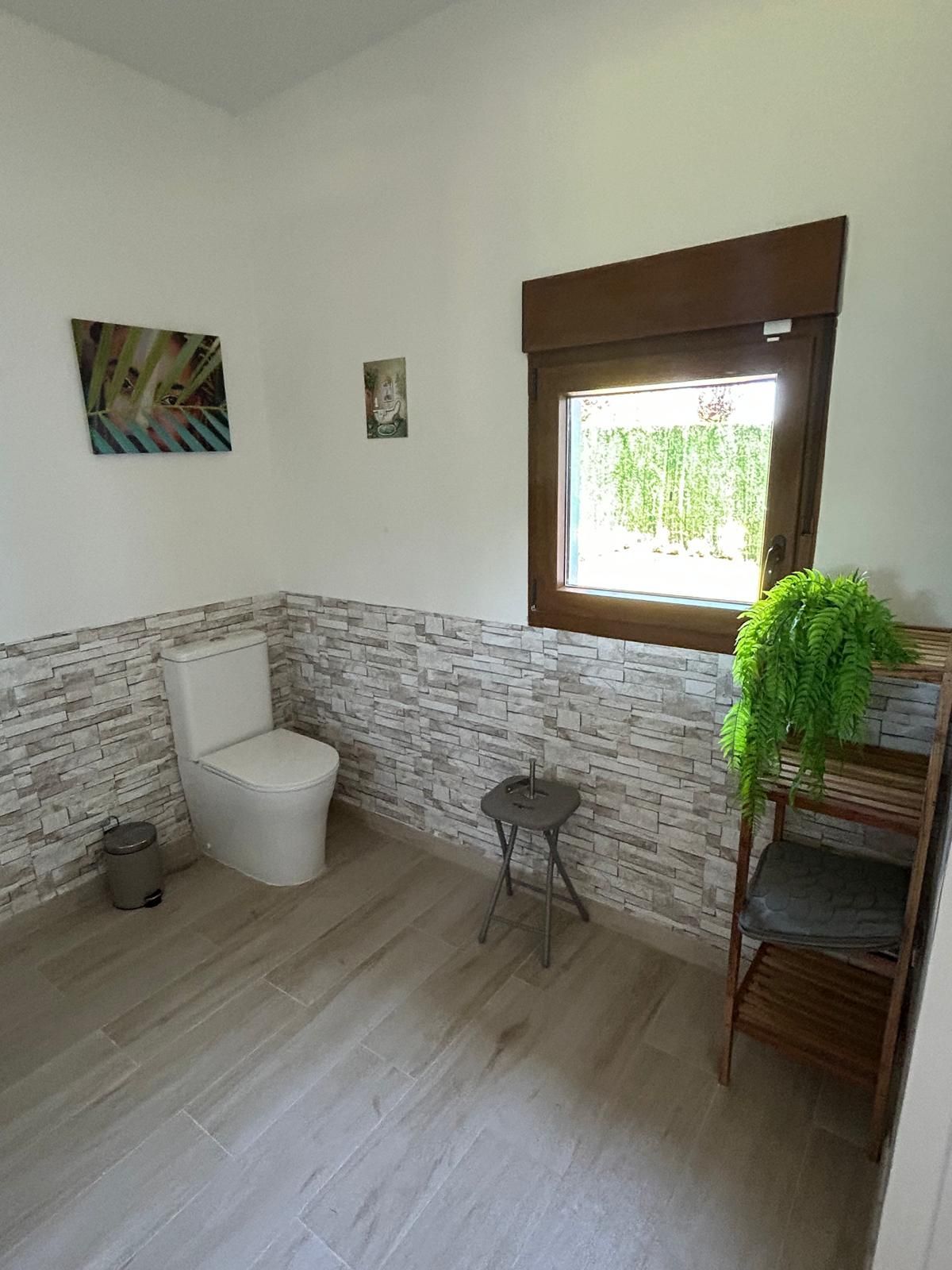 Un baño con inodoro, taburete y ventana.