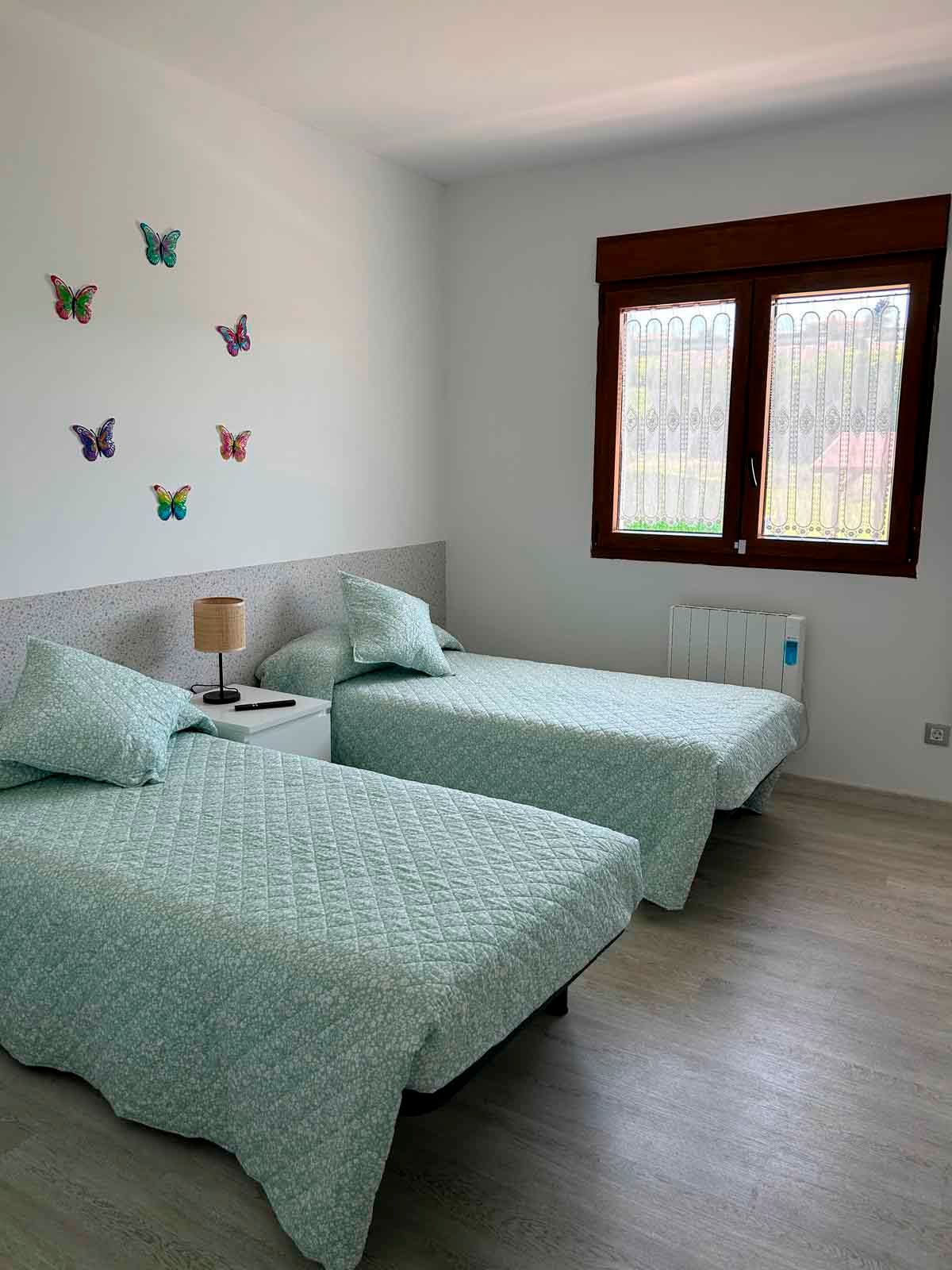 Un dormitorio con dos camas y una ventana con mariposas en la pared.
