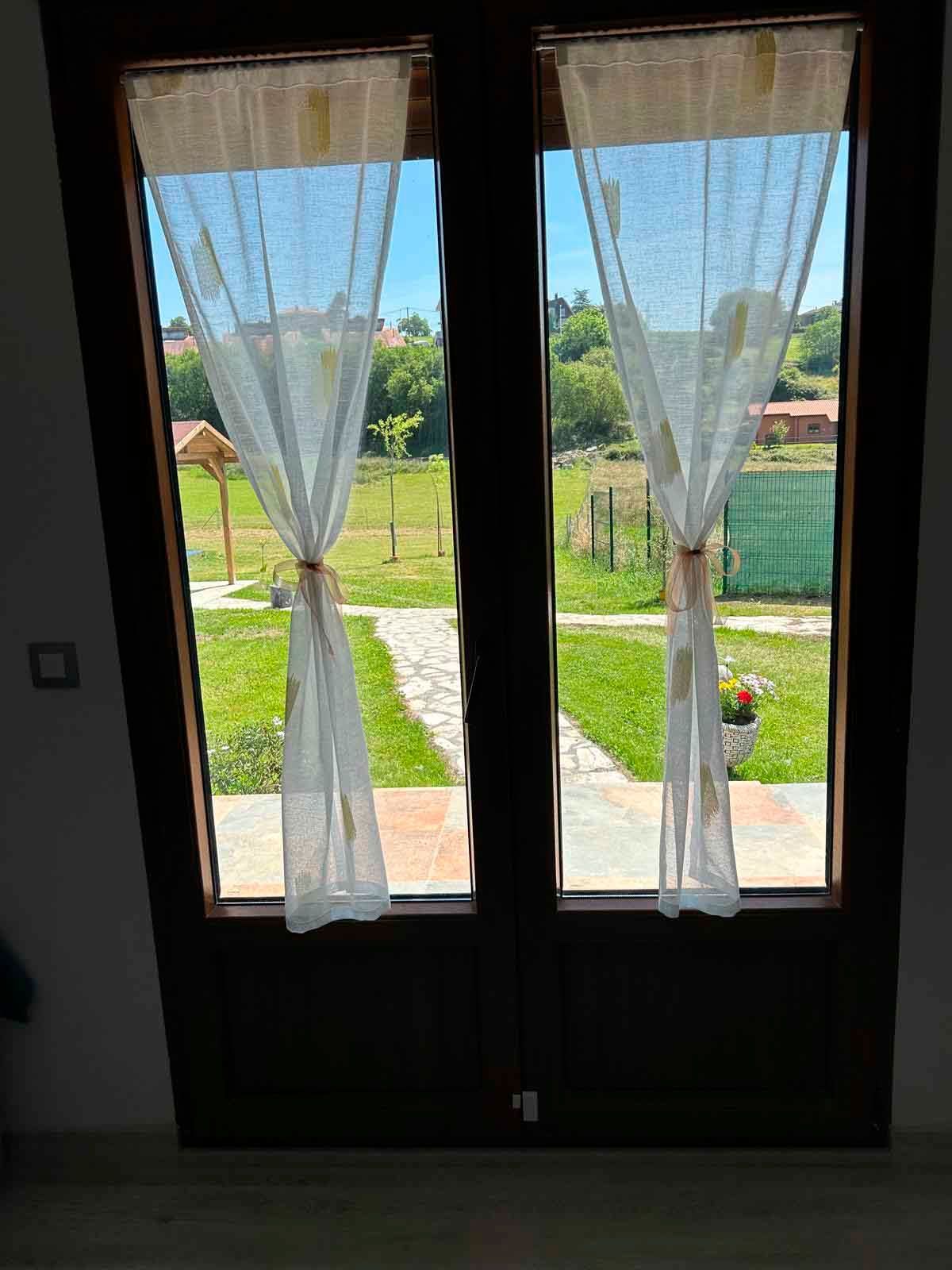 Hay una vista de un campo a través de una ventana con cortinas.