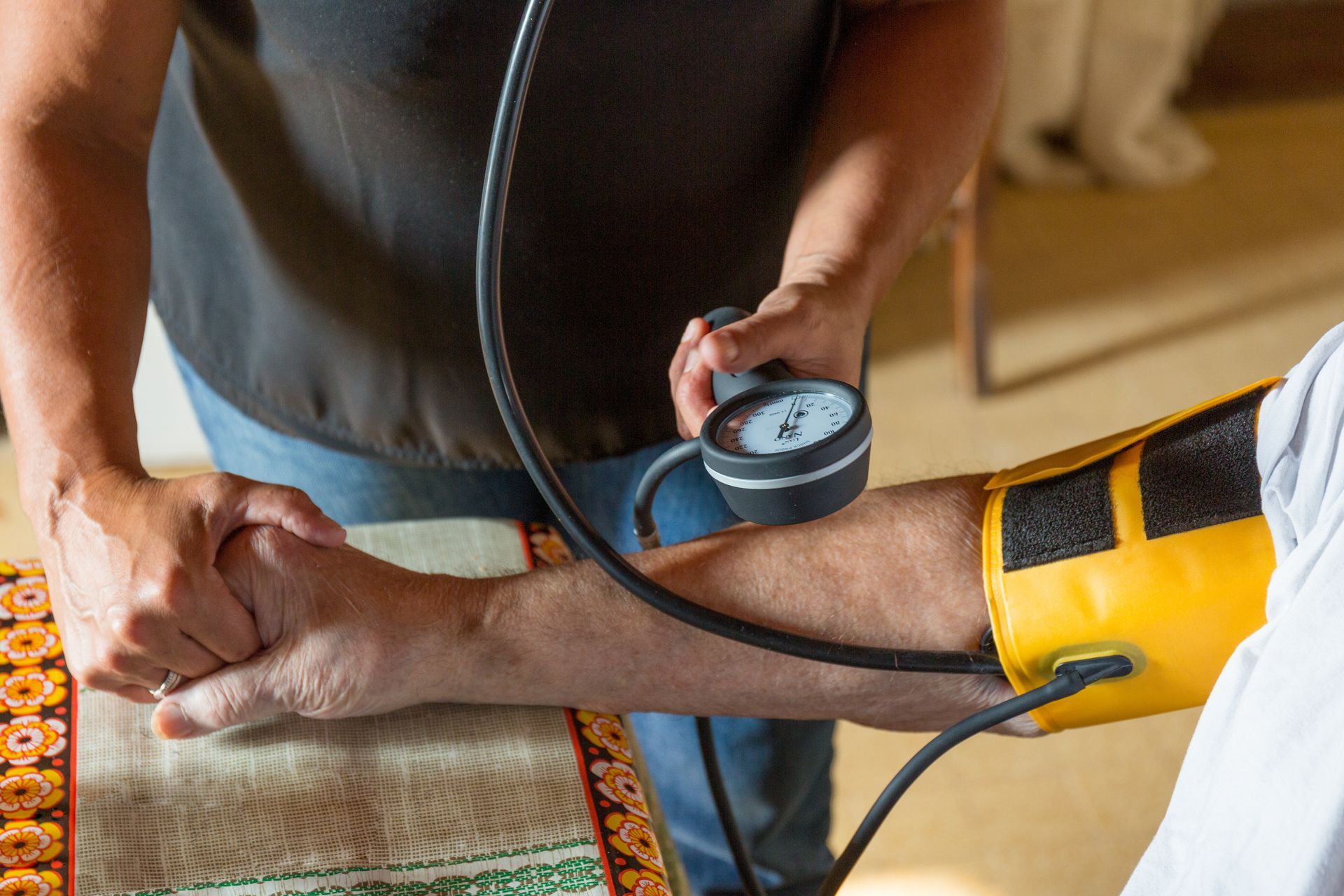 Une personne tenant la main d'une autre tout en utilisant un brassard de tensiomètre manuel sur son bras.