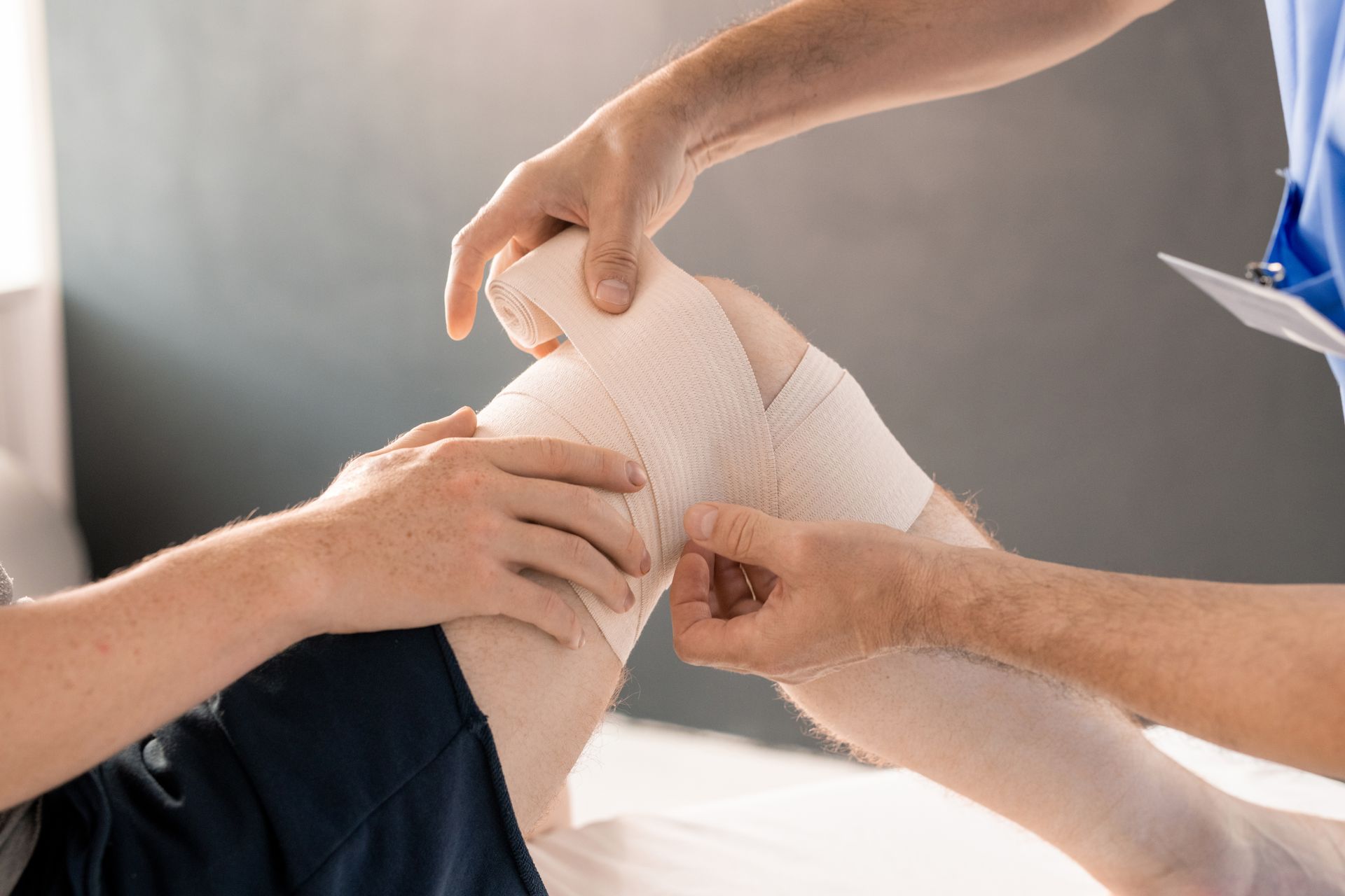Un professionnel de santé applique un bandage compressif beige sur le genou d'un patient.