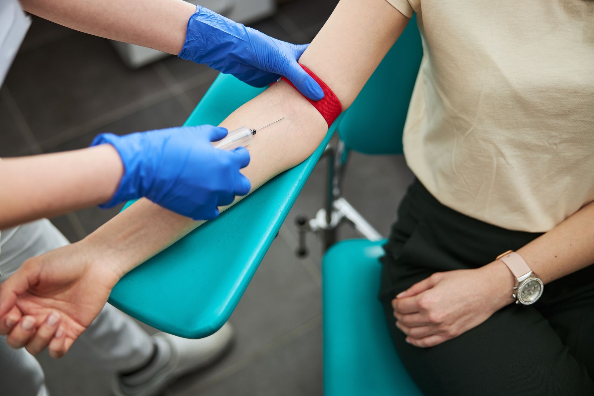 Un agent de santé ganté effectue un prélèvement sanguin sur le bras d'un patient, bras avec un garrot rouge.