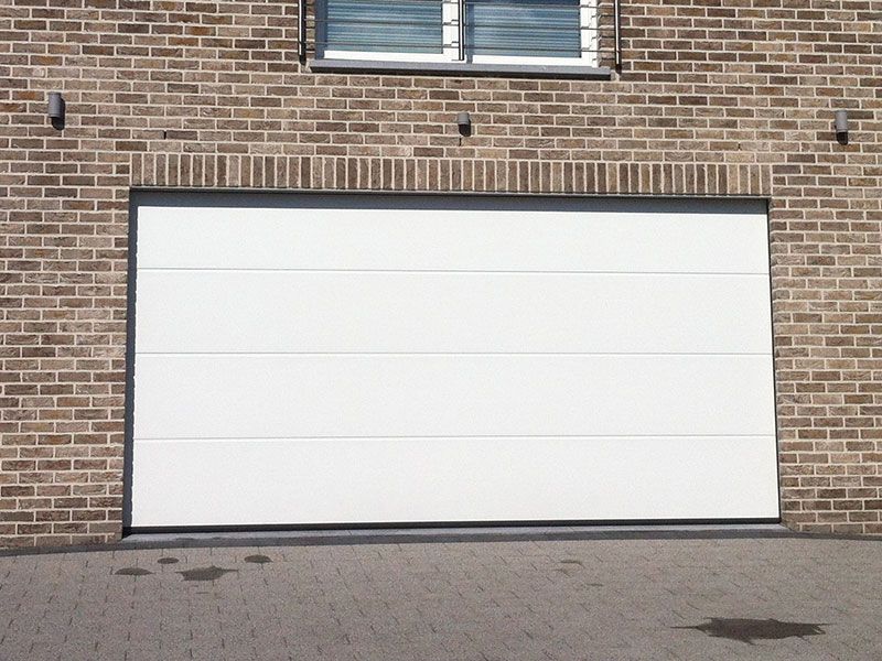 Ein weißes Garagentor steht vor einer braunen Ziegelwand