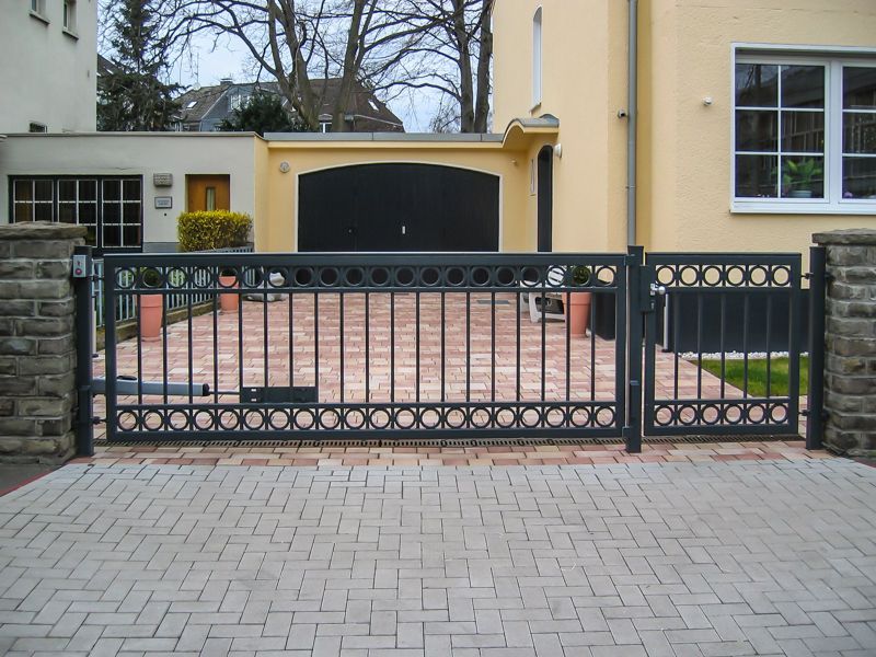 Eine gemauerte Auffahrt mit einem schwarzen Tor, das zu einem Haus führt