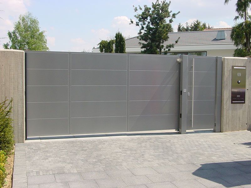 Ein graues Metalltor öffnet sich zu einer Einfahrt vor einem Haus