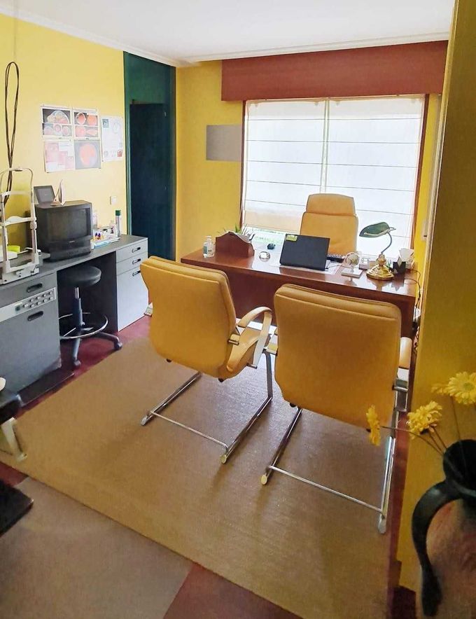 Oficina amarilla con escritorio, dos sillas, ordenador y persianas de colores vivos.