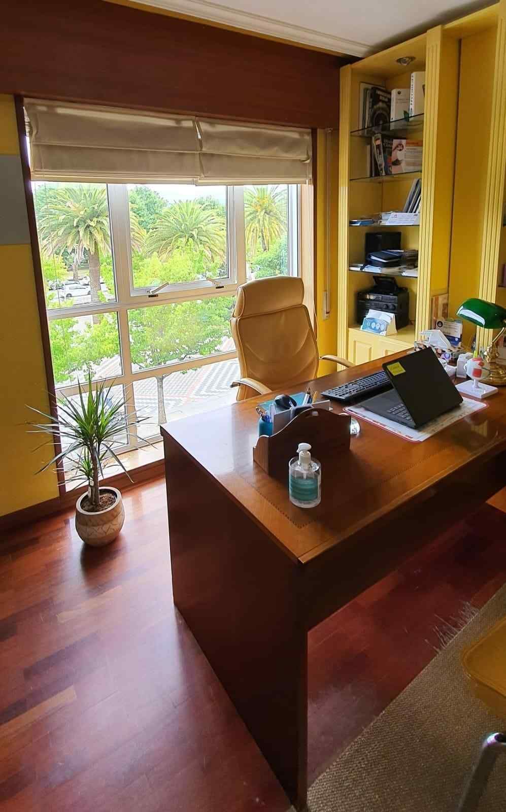 Oficina en casa con escritorio de madera, computadora portátil, silla y una gran ventana con vista a la vegetación.