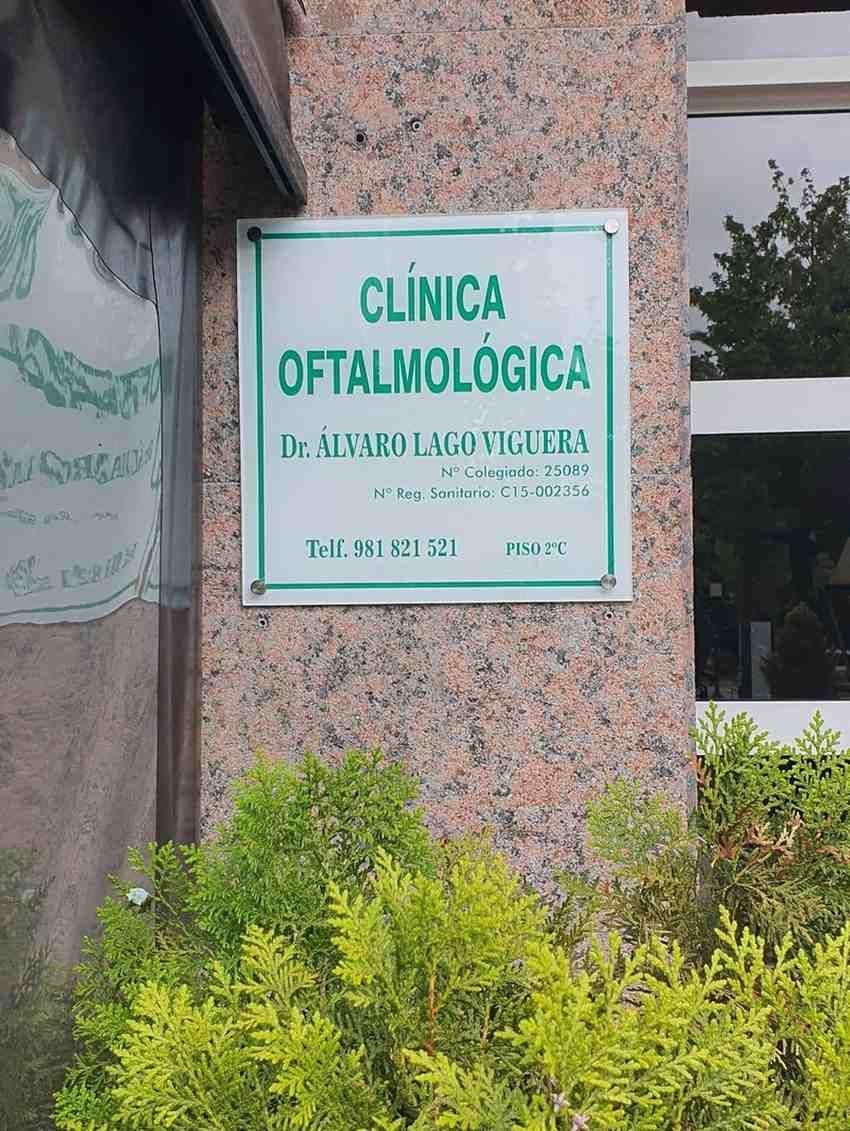 Letrero de una clínica oftalmológica ecológica en un edificio de piedra, con plantas debajo.