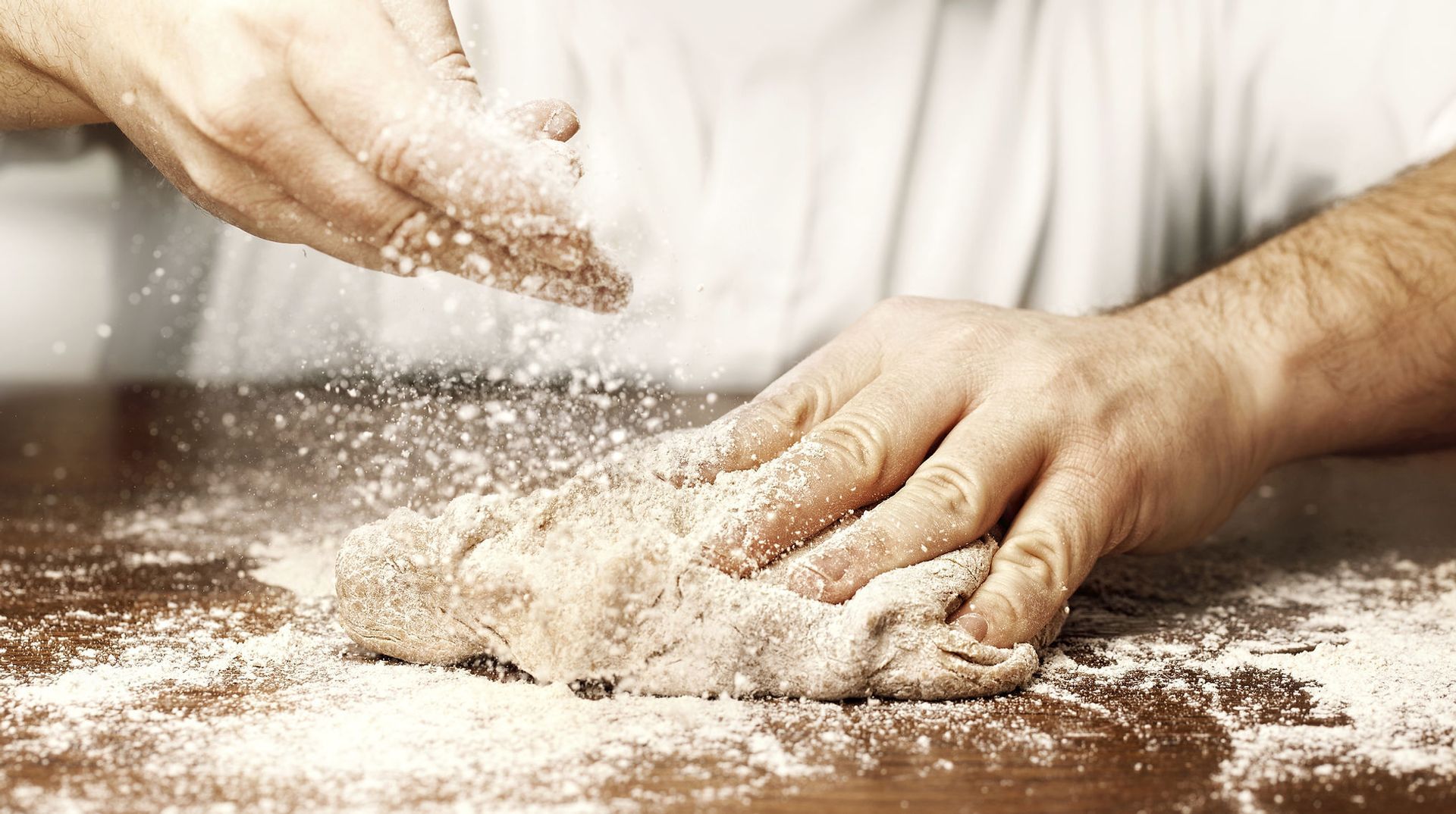 Hände kneten Teig auf einer Holzoberfläche, streuen Mehl darüber und backen Brot.