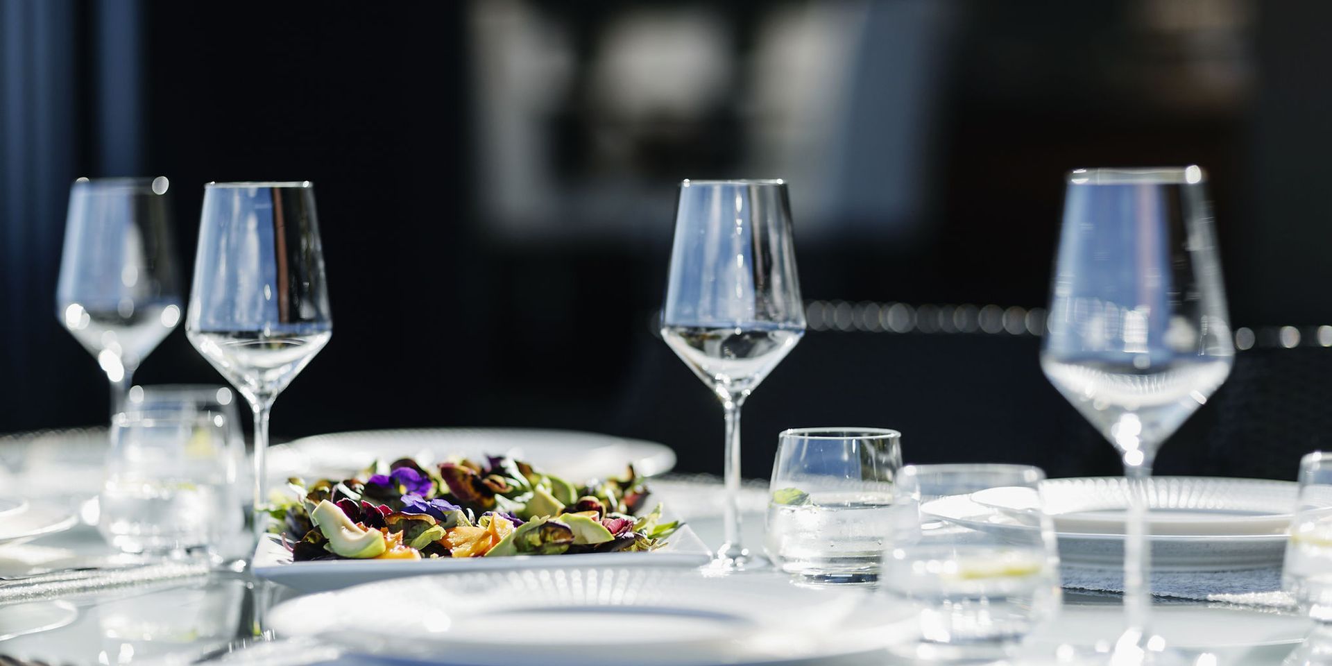 Tischgedeck mit Salat, Weingläsern und Wassergläsern.