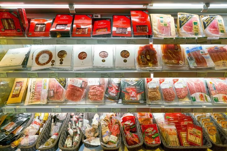 Exhibición de carne de supermercado con cortes rojos envasados, aves y embutidos en estantes refrigerados.