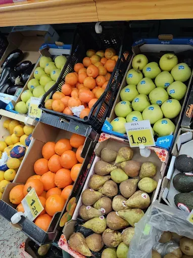 Exhibición de frutas con naranjas, peras, manzanas y uvas en cajas en un supermercado.