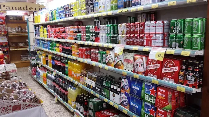 Pasillo de supermercado con estantes repletos de coloridas bebidas y aperitivos enlatados y embotellados.