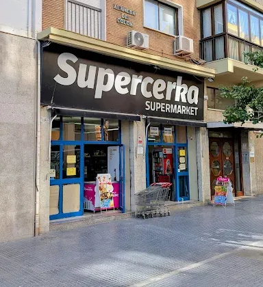 Fachada del supermercado Supercerka con puertas azules y un carrito de la compra en la acera.