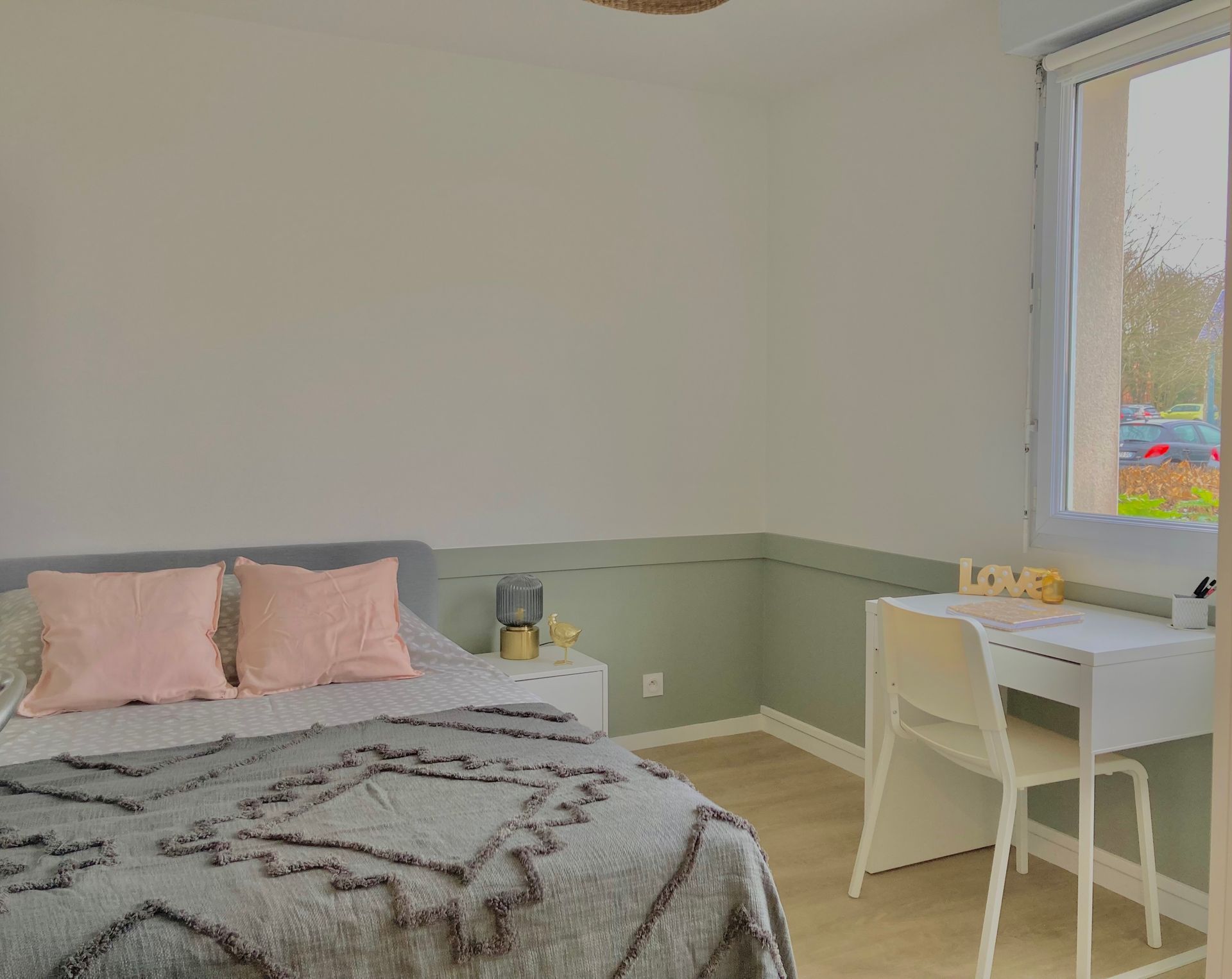 Chambre avec lit, bureau et fenêtre ; murs blancs et verts.