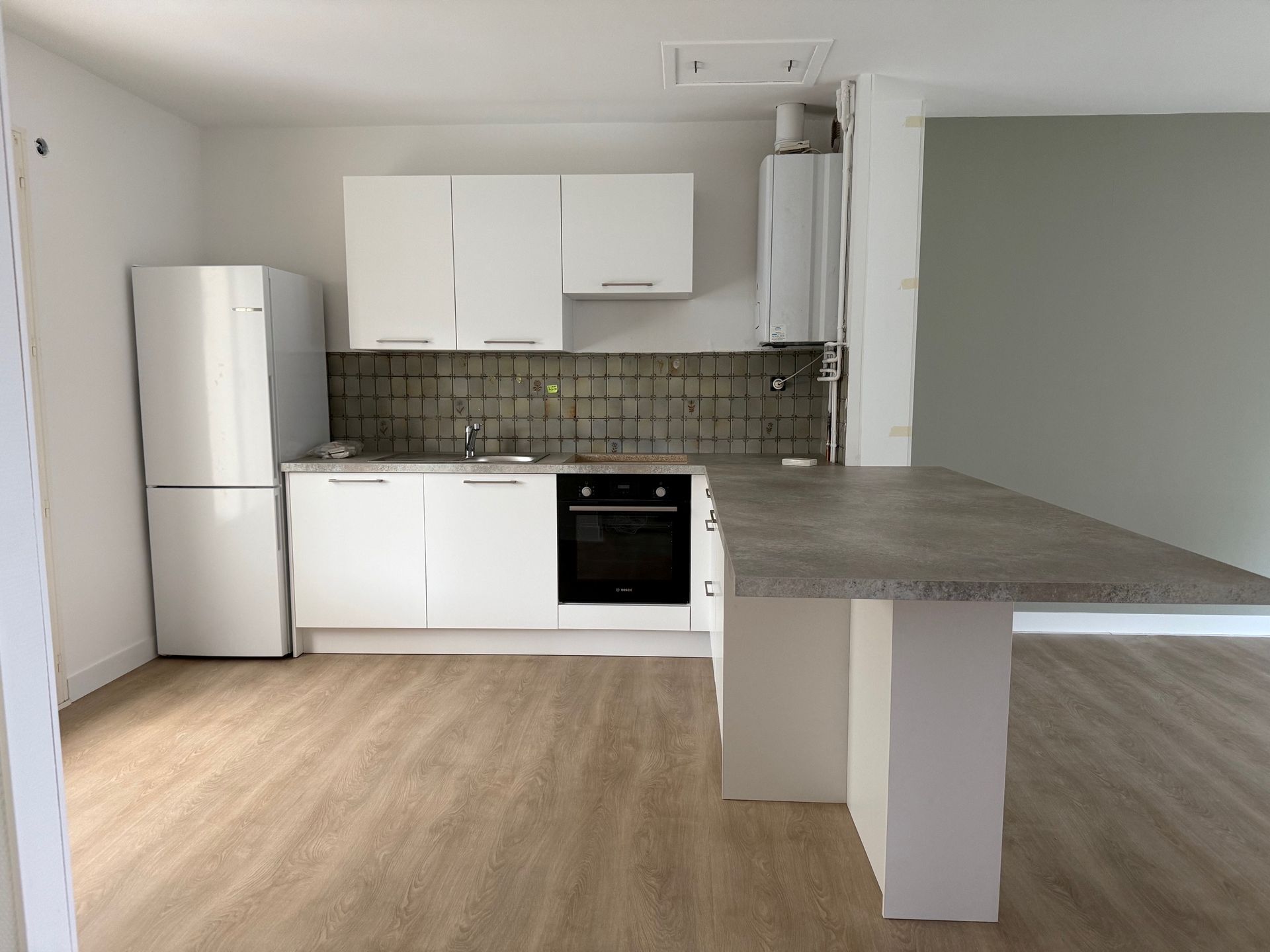 Cuisine blanche moderne avec réfrigérateur, placards, four et îlot central.