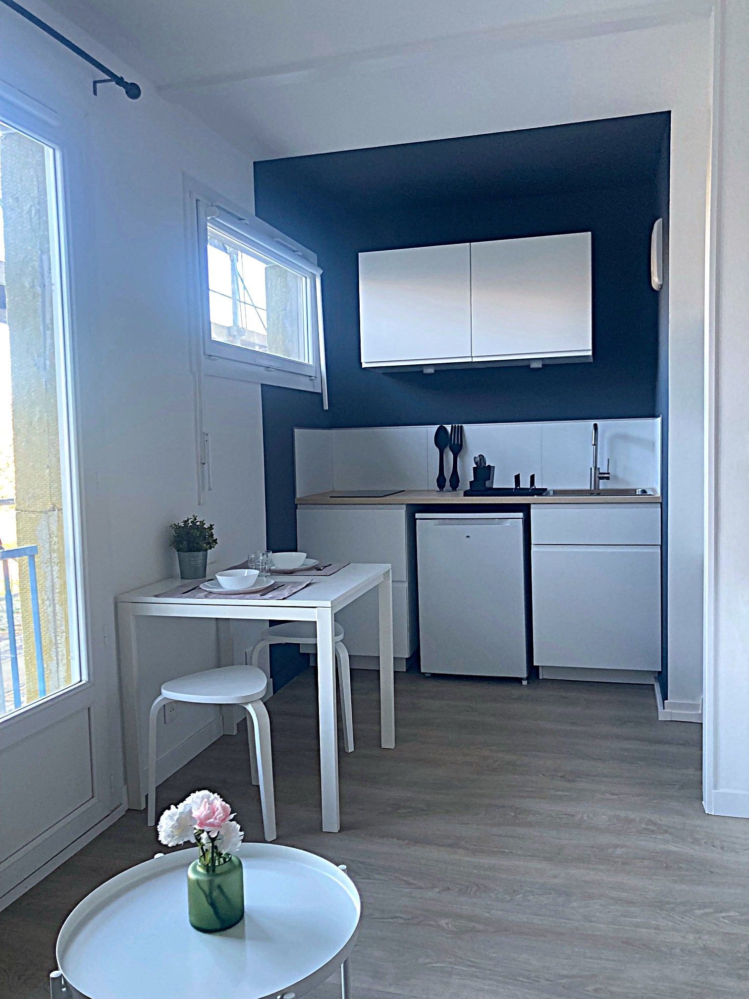 Petit studio avec des touches de blanc et de bleu marine ; une kitchenette et une table avec un tabouret.