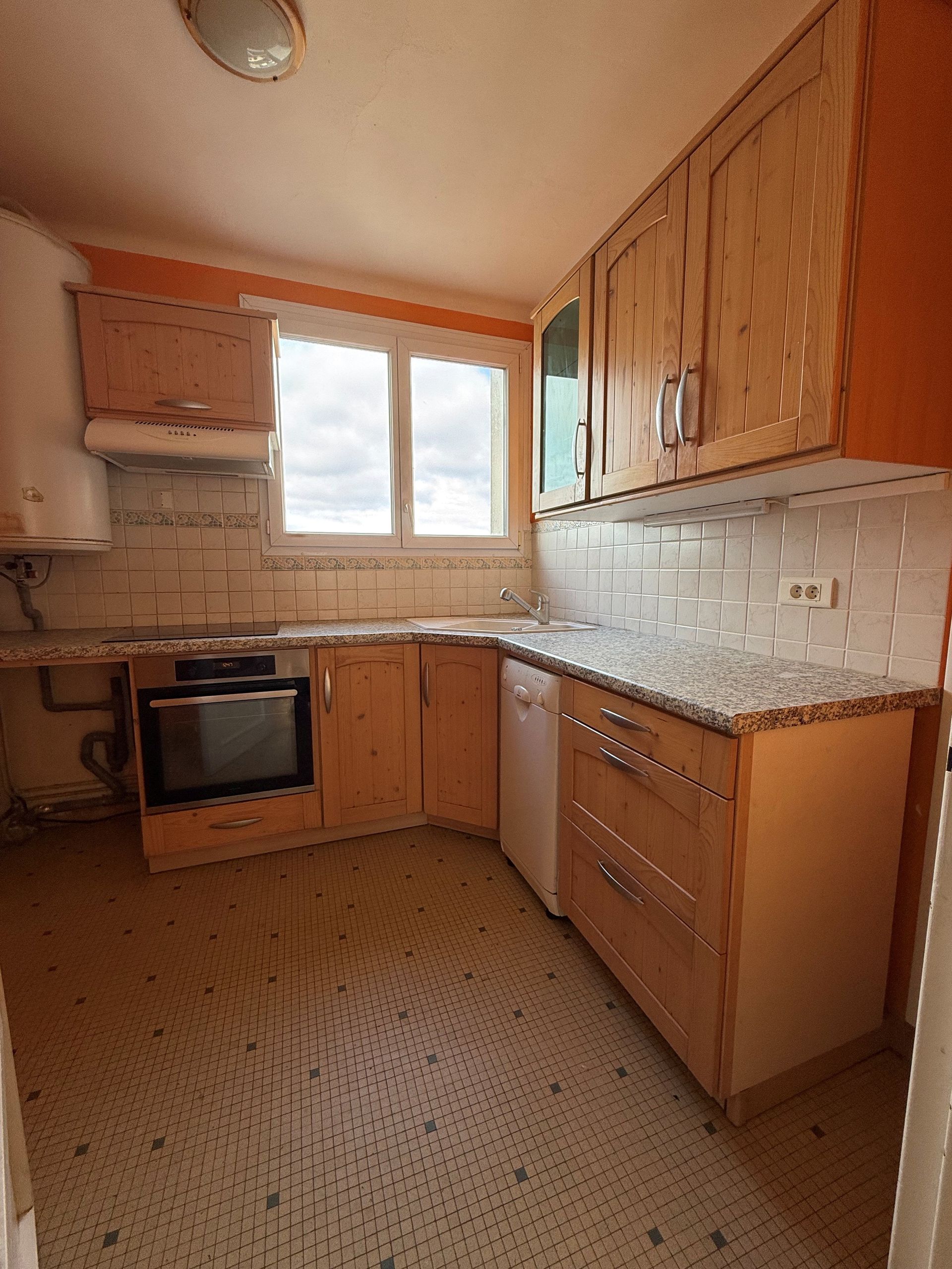 Cuisine en forme de L avec placards en bois clair, comptoirs en granit et crédence carrelée