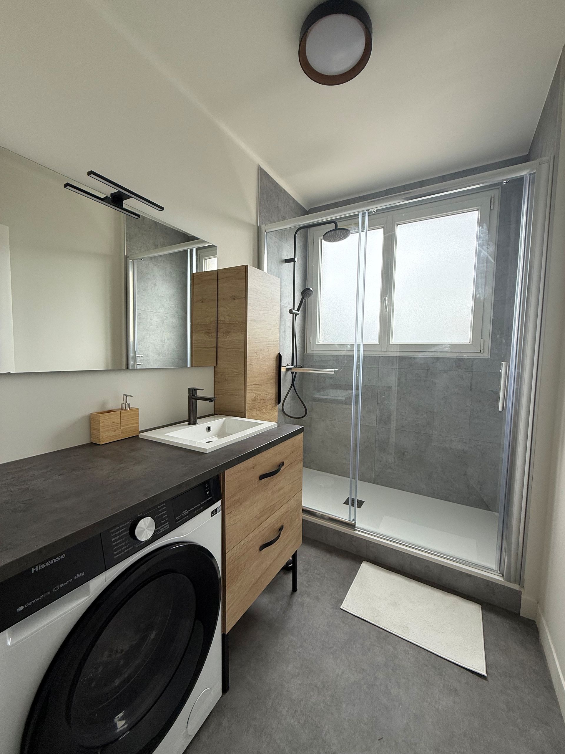 Salle de bains avec lave-linge, lavabo et douche. Décoration grise et bois.