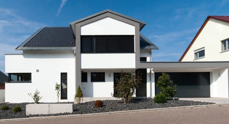 Modernes, zweistöckiges, weißes Haus mit grauem Dach und angebautem Carport. Schwarze Fensterläden, Steingarten.