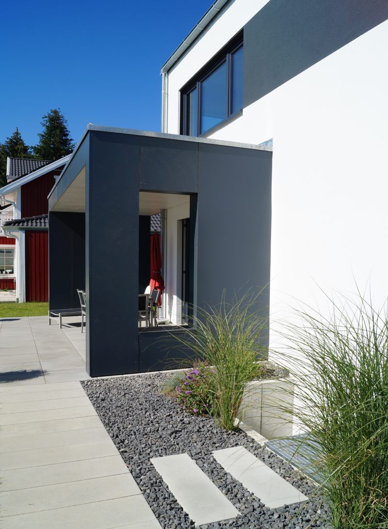 Modernes Haus mit grauem Eingangsbereich, weißer Fassade und Trittsteinen.