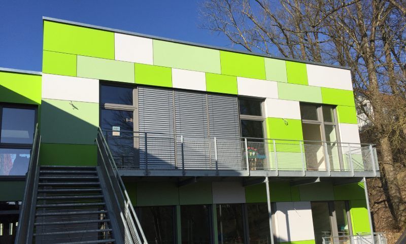 Ein grün-weiß gefliestes Gebäude mit Fenstern und einer Metalltreppe.