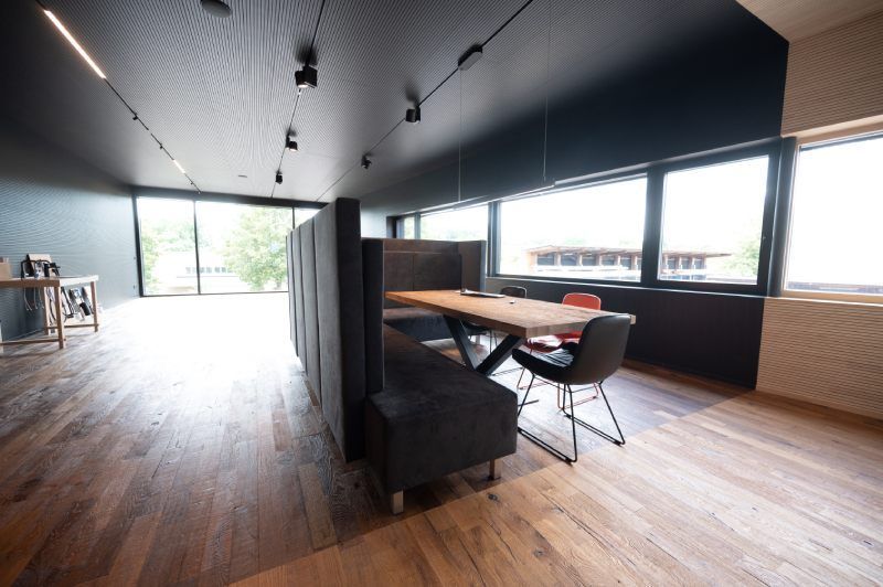Modernes Büro mit großem Holztisch, Sitznischen und großen Fenstern.