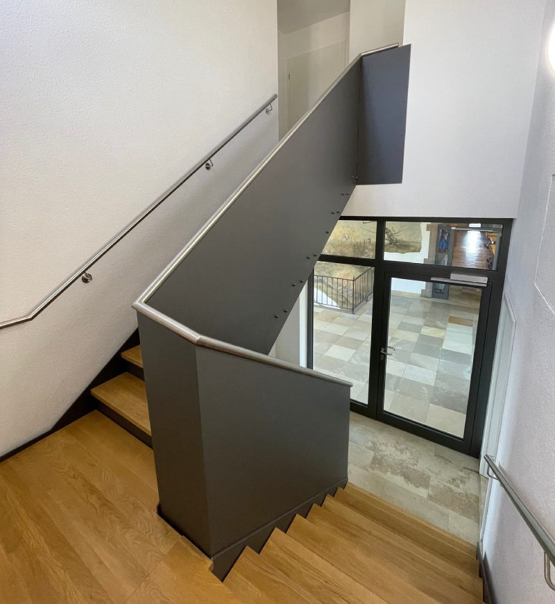 Treppe mit Holzstufen, grauem Metallgeländer und einem Fenster am unteren Ende.