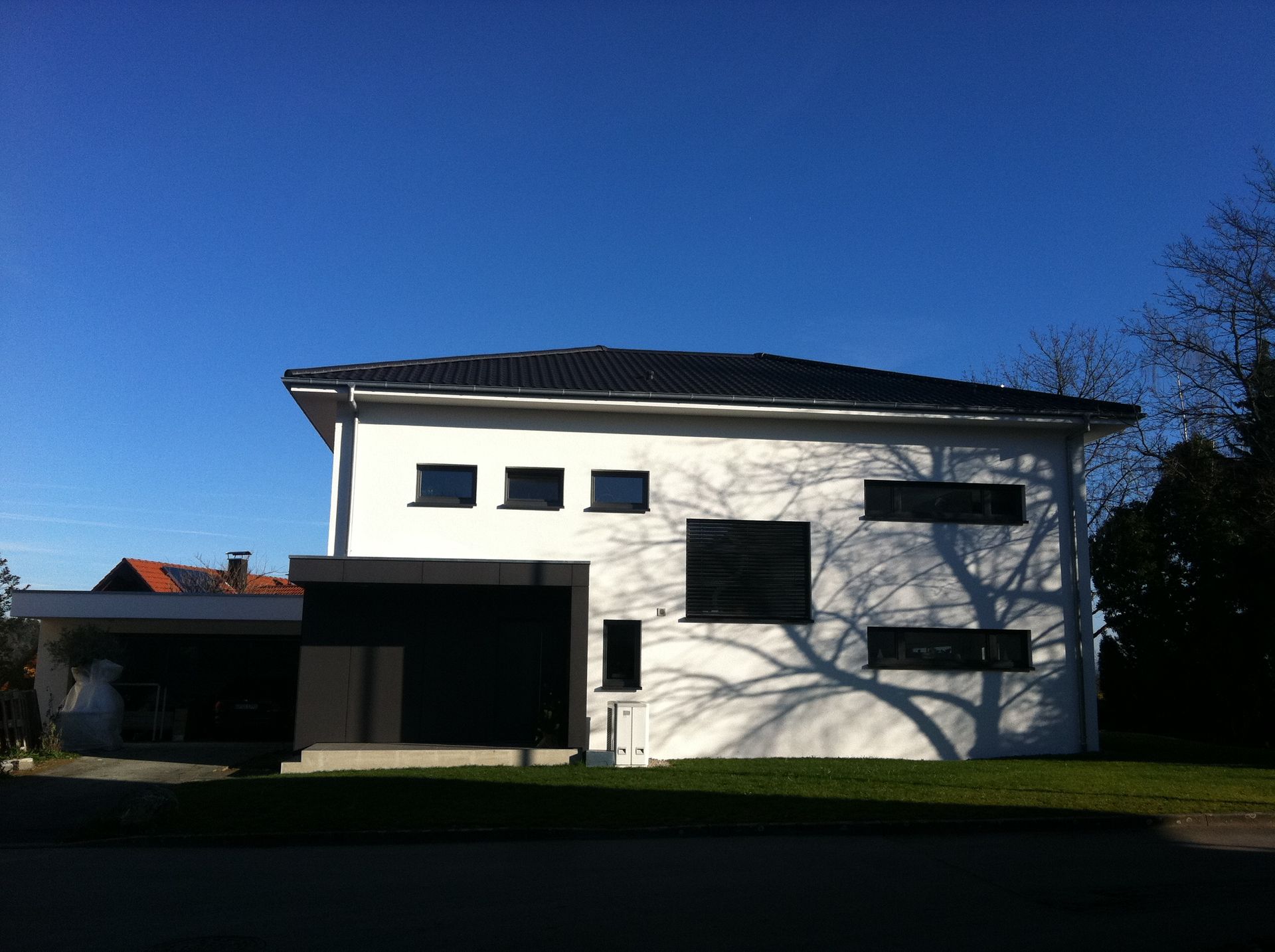 Modernes weißes Haus mit Flachdach, schwarzen Fenstern und Carport an einem sonnigen Tag.