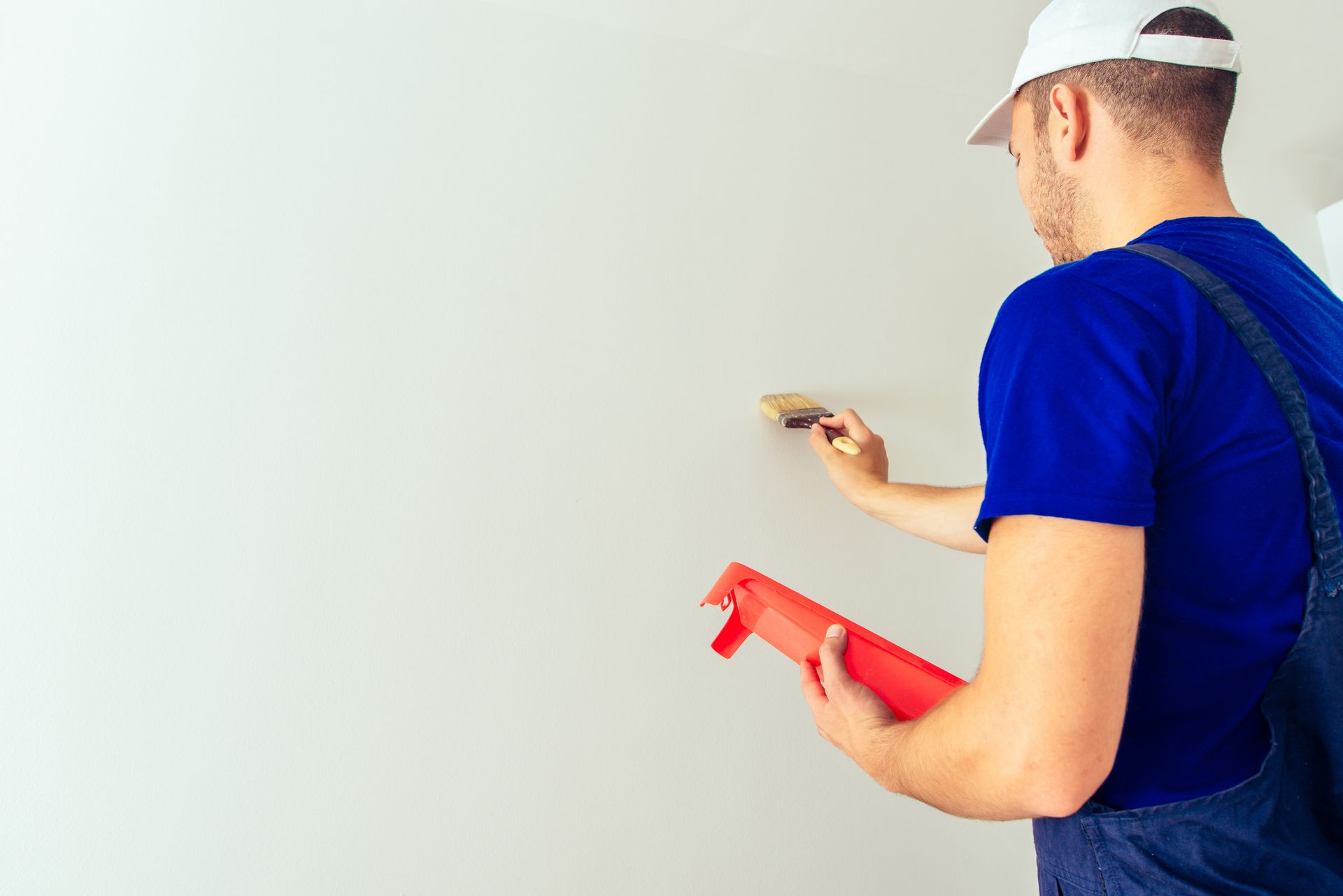 Pintor con mono azul y sombrero blanco, pintando una pared con un pincel.