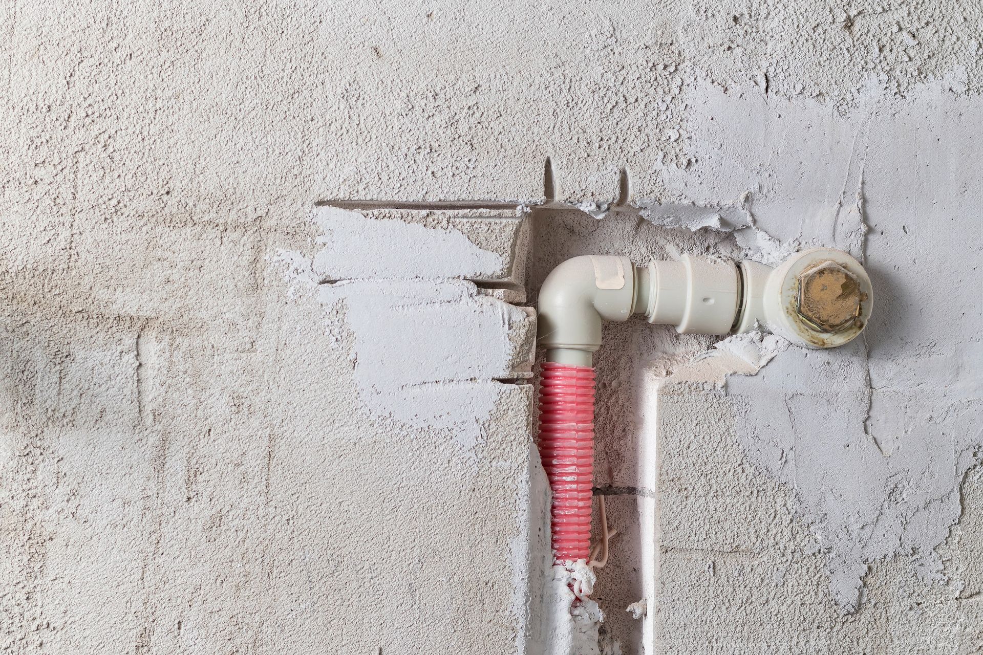 Las tuberías de plomería de color blanco y tostado están incrustadas en una pared texturizada de color blanquecino.