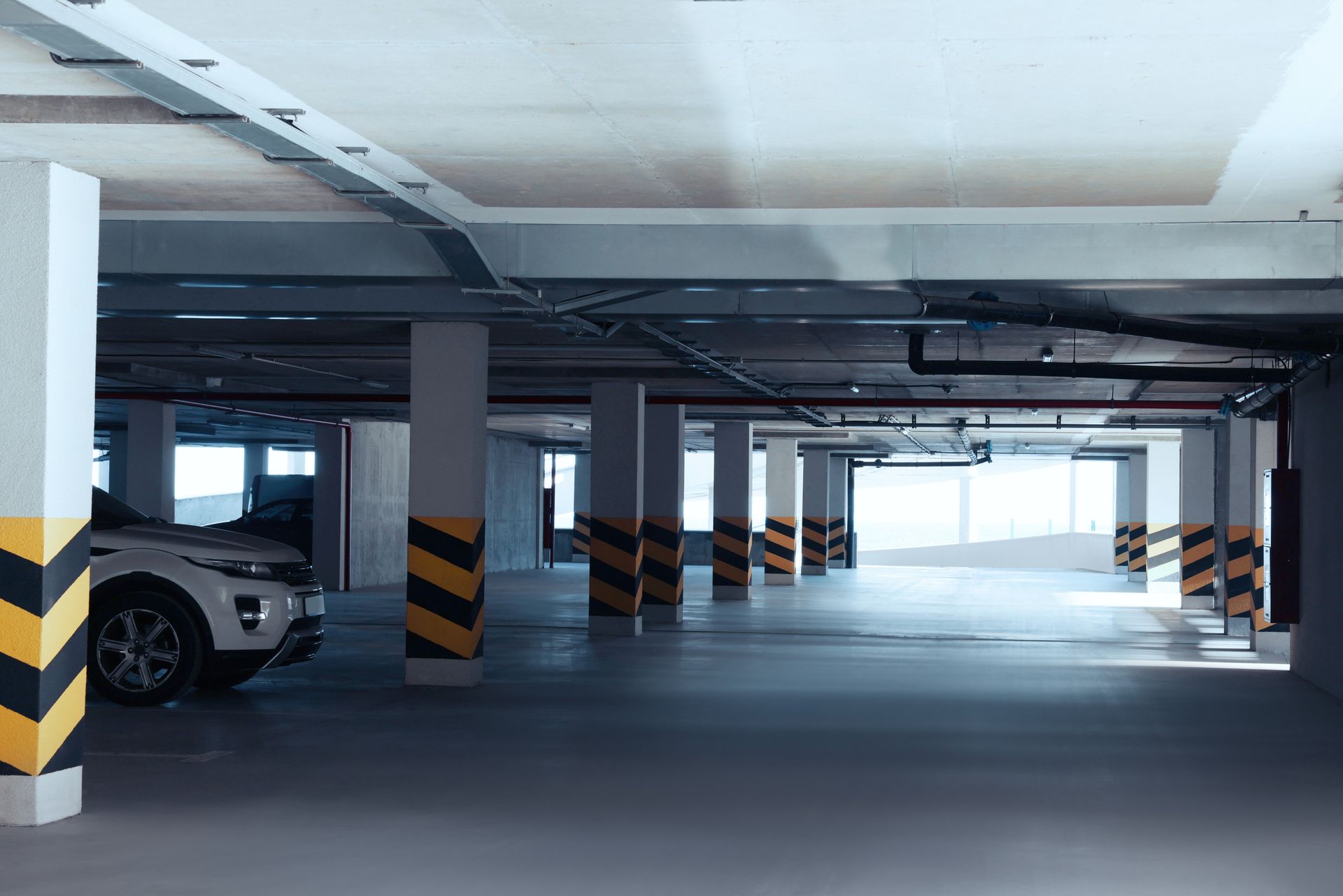 Aparcamiento subterráneo con un coche blanco aparcado a la izquierda. Columnas pintadas de negro y amarillo.